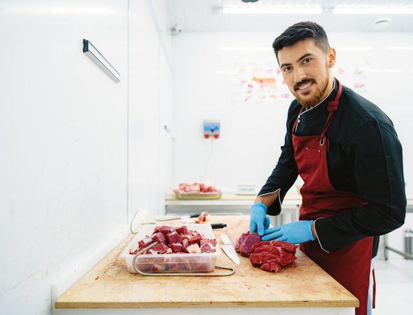 Butcher cutting slices of raw meat on wooden board, close up